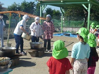 5歳児らいおん組が園庭のかまどの鍋でいも汁を作る様子を見ている写真