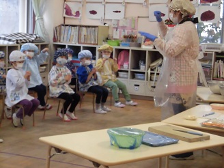 4歳児（ぱんだ組）が調理活動前に説明を聞いている写真