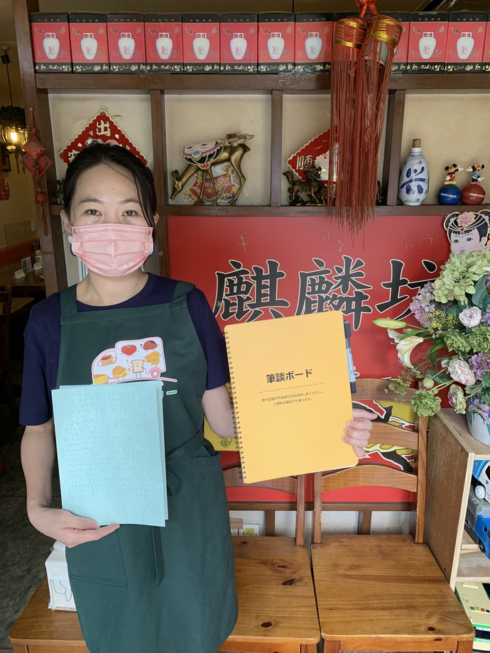 中国家庭料理麒麟坊の従業員が筆談ボードと点字メニューを持っている写真