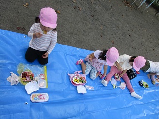 2歳児うさぎ組が園庭でお弁当を食べている様子の写真