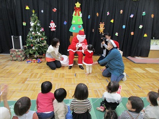 サンタクロースにプレゼントをもらう1歳児りす組の子どもたちの様子の写真