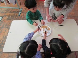 写真：3歳児　箸を使い、お皿からマカロニを取ろうとしている様子