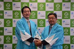 写真：新撰組のだんだら模様の羽織り姿で握手する市長と支店長