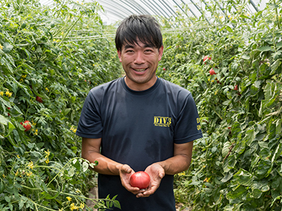 写真：収穫したトマトを持つ笑顔の天野　武雄さん