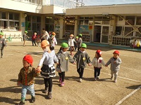 保育園と幼稚園の年長児が1歳児と手をつないで歩いている様子