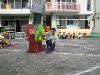 1歳児（りす組）が段ボールで作ったどんぐりの木でどんぐりをとっている写真