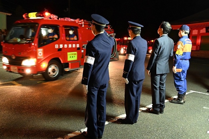 写真：団長、市長、第九消防方面本部長、消防署長が車両を見送っている様子。