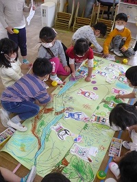 4歳児ぞう組の子どもたちがおかしどろぼうのこびとの塗り絵を台紙に貼っている写真