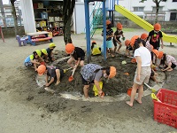 5歳児が泥んこ遊びをして川に水を流している写真です。