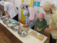 5歳児ぞう組の子どもたちが担任や調理員さんと一緒に、食材を切っている写真