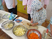 5歳児ぞう組の子どもたちが担任や調理員さんと一緒に、食材を切っている写真