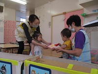 1歳児うさぎ組の子どもが0歳児ひよこ組の誕生児に誕生カードを渡している写真