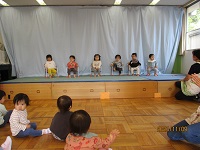 0歳児ひよこ組の子どもたちが舞台でCDに合わせて手遊びをしている写真