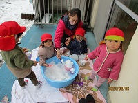 1歳児うさぎ組の子どもたちがタライに雪を入れて遊んでいる写真
