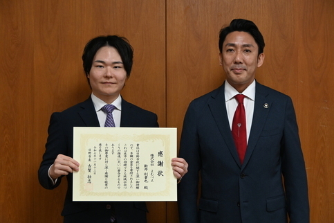 感謝状贈呈式にて、賞状を持つ株式会社よむべえ代表あらいりきや様と日野市長