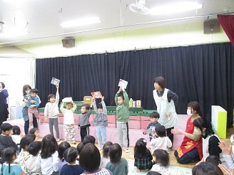 11月の誕生児の子ども達が誕生会で、誕生日カードを掲げている様子の写真