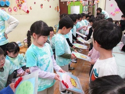 幼児クラスの友達が卒園児にクリアファイルのプレゼントを渡しているところ