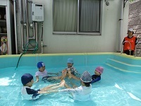 写真:5歳児がプール内で足を伸ばして輪になって座り、V字バランスに挑戦している様子