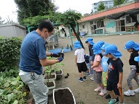 写真：子ども達が用務員さんから苗の植え方の説明を受けている様子